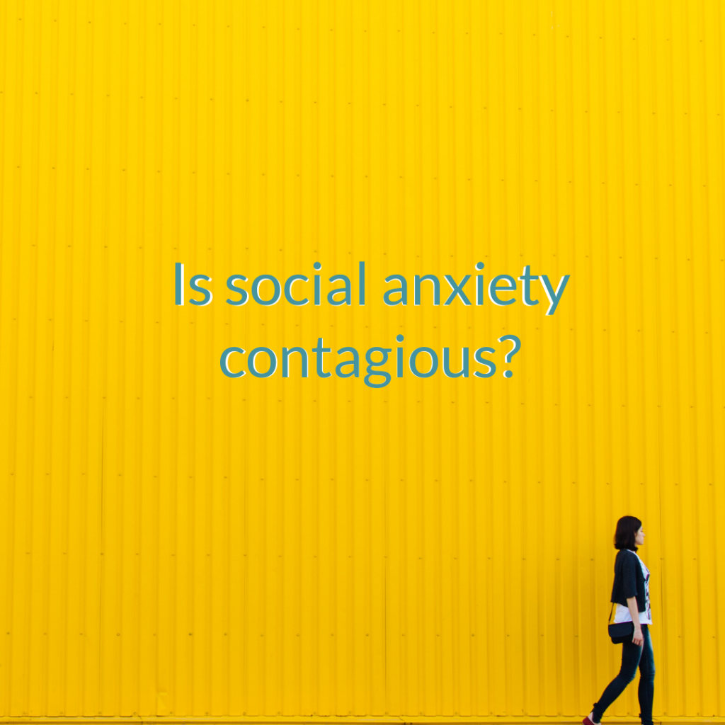 a single person walks alongside a large yellow wall. On the wall reads 'is social anxiety contagious'